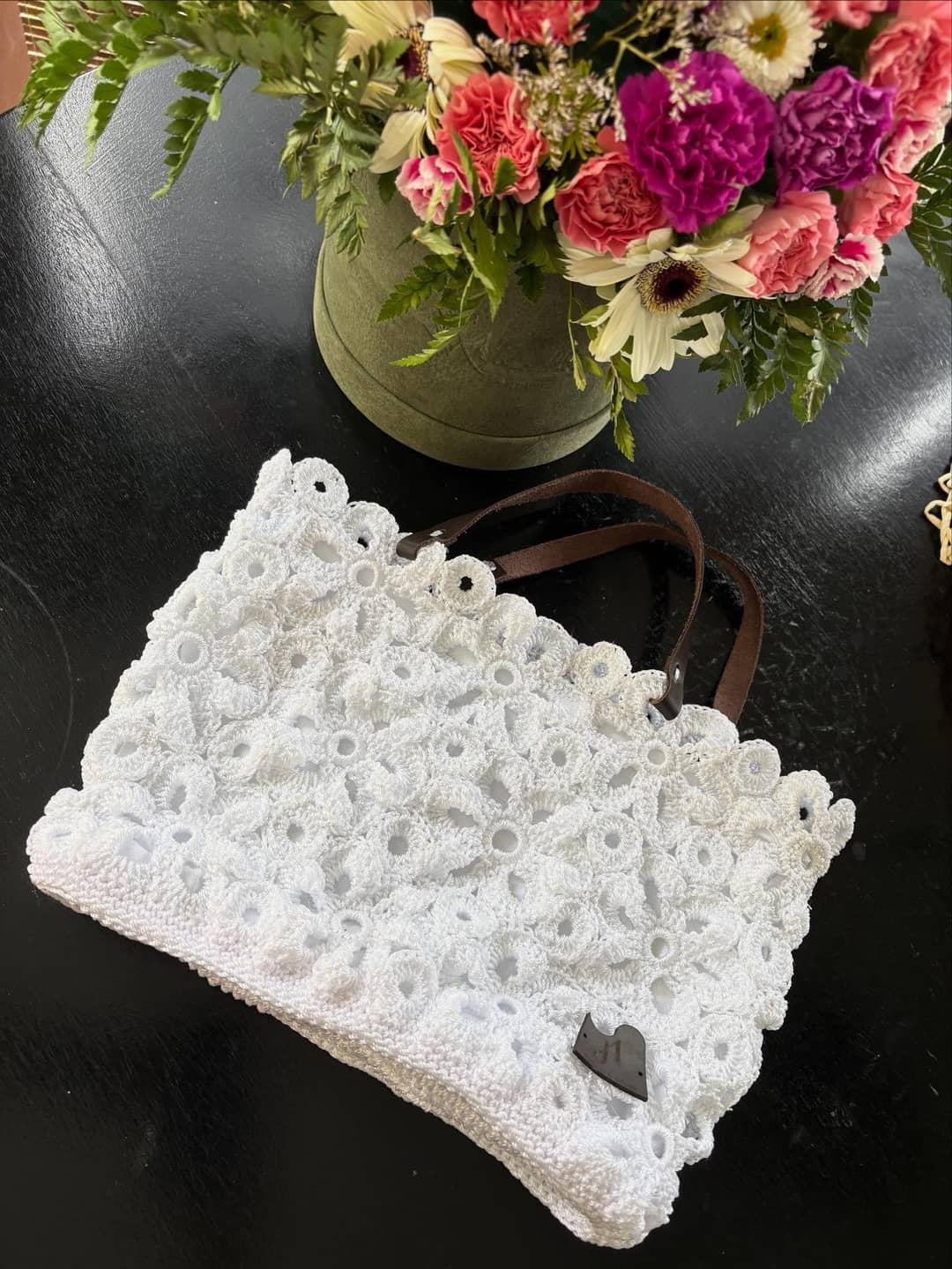 Cartera blanca calada con flores de fondo.